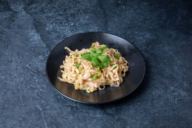 spaghetti with chicken and vegetables in a plate on a black background. top view.