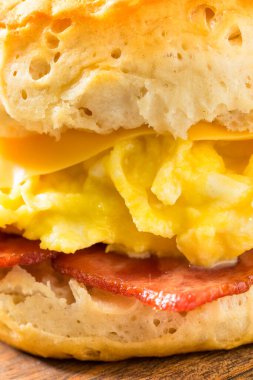 Kahvaltı için yağlı pastırmalı yumurta ve peynirli tereyağlı bisküvili sandviç.