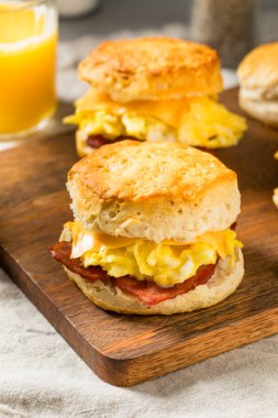Kahvaltı için yağlı pastırmalı yumurta ve peynirli tereyağlı bisküvili sandviç.