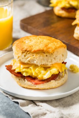 Kahvaltı için yağlı pastırmalı yumurta ve peynirli tereyağlı bisküvili sandviç.