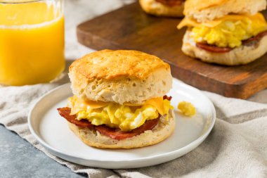 Kahvaltı için yağlı pastırmalı yumurta ve peynirli tereyağlı bisküvili sandviç.