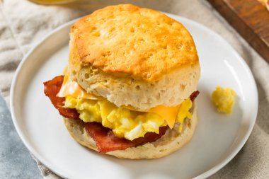 Kahvaltı için yağlı pastırmalı yumurta ve peynirli tereyağlı bisküvili sandviç.
