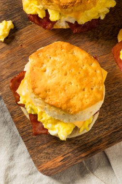 Kahvaltı için yağlı pastırmalı yumurta ve peynirli tereyağlı bisküvili sandviç.