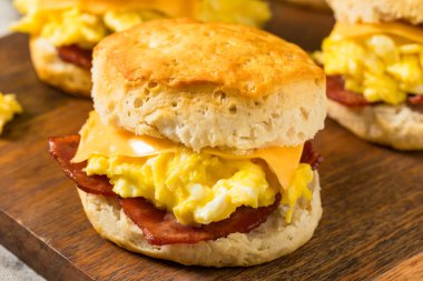 Kahvaltı için yağlı pastırmalı yumurta ve peynirli tereyağlı bisküvili sandviç.