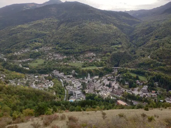 Görkemli bir dağ sırası sakin bir vadiye bakıyor, yemyeşil bitkiler ve ağaçlar huzurlu bir ortam yaratıyor..