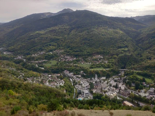 Görkemli bir dağ sırası sakin bir vadiye bakıyor, yemyeşil bitkiler ve ağaçlar huzurlu bir ortam yaratıyor..