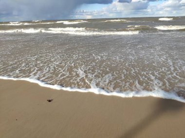 Gündüz vakti kar bulutları ve mavi gökyüzü olan kış kumsalı