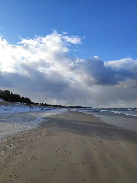 Gündüz vakti kar bulutları ve mavi gökyüzü olan kış kumsalı