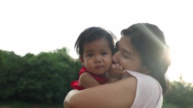 Annesiyle oynayan küçük kız mutlu kucaklaşmalar ve yanaklarından öpücükler, Tayland 'lı genç anne parkta bebeği tutuyor, mutlu aile çocuğu yaşam tarzı rüya kavramı