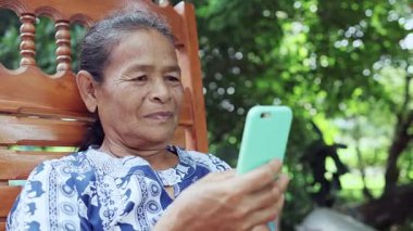 Mutlu Asyalı yetişkin kadın video ve yüz araması ile rahatlıyor, ailesiyle cep telefonuyla konuşuyor, thai asia yaşlı büyükannesi kablosuz teknoloji cihazıyla açık hava yaşam tarzının keyfini çıkarıyor.