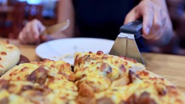Lokantadaki kadın tabağına bir dilim peynirli pizza servis etmek için pizza kesicisi kullanıyor. Lezzetli, yeni pişmiş bir pizzayı yakından görüyor.