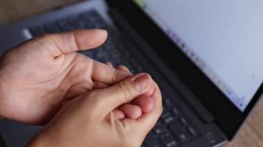 Parmak uçlarında uyuşukluk, arka planda dizüstü bilgisayarla elleri sıkan uyuşuk parmaklar. El uyuşukluğu, sinir ağrısı, karpal tünel sendromu veya aşırı bilgisayar kullanımından kaynaklanan ofis sendromu kavramı.