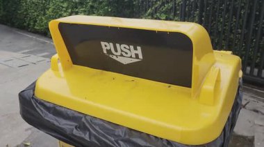 Çöp kutusuna plastik şişe atmak, çöp kovası, bahçedeki sarı geri dönüşüm plastik kutusu, yakın çekim, tekerlek kutusu, çöp ve atık için PUSH sembolü olan çöp kutusu.