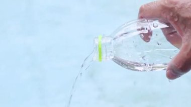 hand pouring water from a plastic bottle, symbolizing hydration, purity, water usage, refreshment, or environmental awareness, close-up