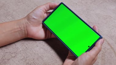 Yatay konumda yeşil ekranlı akıllı telefonu tutan eller, özel içerik ya da model eklemek için idealdir, teknoloji ve reklam kullanımı için tarafsız bir yüzeyde çekilir, yakın çekim