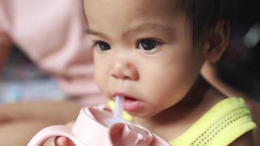 Bebek kendi başına biberonundan su içiyor. erken çocukluktaki kişisel bakım, susuzluk ve sağlıklı alışkanlıkları gösteren sevimli ve sakin bir an, yakın plan, sağlıklı bir an.