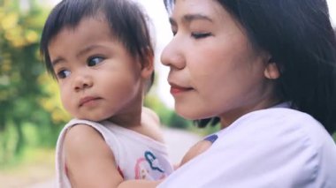 Annesiyle oynayan küçük kız mutlu kucaklaşmalar ve yanaklarından öpücükler, Tayland 'lı genç anne parkta bebeği tutuyor, mutlu aile çocuğu yaşam tarzı rüya kavramı