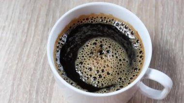 Beyaz fincanda sıcak sade kahve, sıcak kahve, köpüklü kahve ve ahşap masa arkası manzarası. İçecek tasarımı ve kafe reklamı için mükemmel, yakın plan.