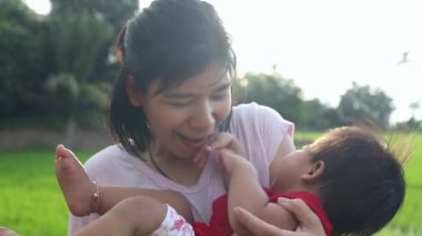 Küçük kız annesiyle oynaşıyor, mutlu sarılıyor ve göbeğini öpüyor. Tayland 'lı genç anne, o parkta gülerken ve mutlu bir şekilde bebeğini kucağına alıp kaldırıyor.