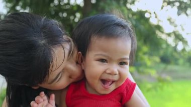Annesiyle oynayan küçük kız mutlu kucaklaşmalar ve yanaklarından öpücükler, Tayland 'lı genç anne parkta bebeği tutuyor, mutlu aile çocuğu yaşam tarzı rüya kavramı