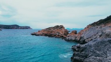 Mavi deniz suyuyla kayalık kayalıkları kayalık kıyı şeridi boyunca ilerleyin.