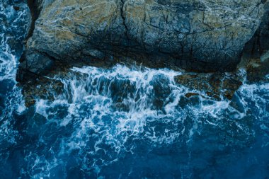 Sahil şeridinde mavi dalgalarla deniz kayalıkları kıyısı, aşağı hava manzaralı.
