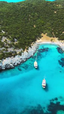 Mavi deniz lagünü ve Ege kıyısı boyunca uzanan yatların havadan görünüşü. Türk Riviera doğasının manzarası. Dikey video