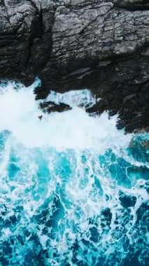 Üst manzara okyanus mavi dalgaları kayalıklara çarpar kıyı şeridi uçurumuna, dikey drone görüntüsü