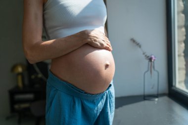 Hamile kadın karnına hafifçe dokunuyor, yeni doğmuş bir bebeği bekleyen kadın.