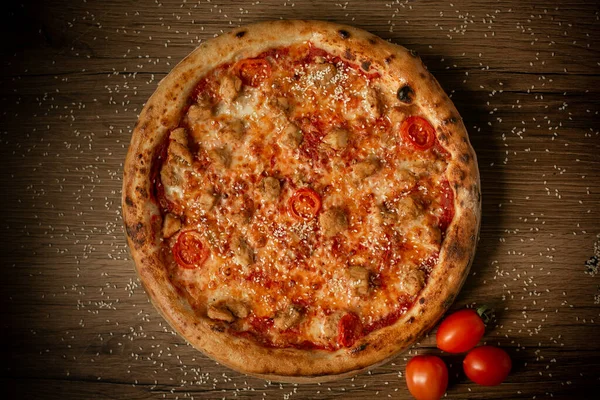 Tavuk ve kiraz domatesli lezzetli pizza, susam tohumları serpiştirilmiş, üst manzara. koyu tahta masa arkaplanı alçak tuş