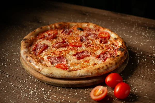 delicious pizza with chicken and cherry tomatoes, sprinkled with sesame seeds, dark wooden table background low key