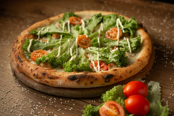 delicious chicken pizza with salad leaves and cherry tomatoes, dark wooden table background low key