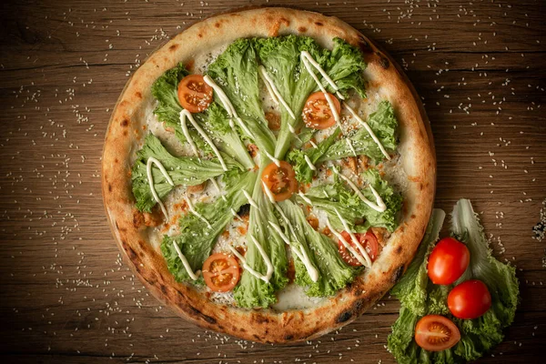 delicious chicken pizza with salad leaves and cherry tomatoes top view. dark wooden table background low key