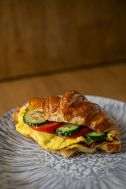 Sebzelerle dolu bir kruvasan. Salatalık domates ve yumurta omleti. Ahşap bir arka planda gri bir tabakta.