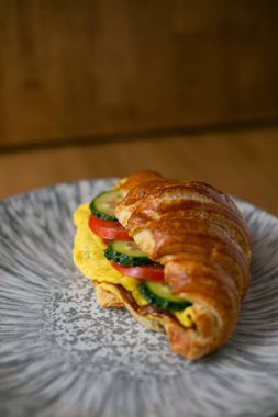 Sebzelerle dolu bir kruvasan. Salatalık domates ve yumurta omleti. Ahşap bir arka planda gri bir tabakta.