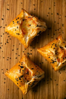 Tahta arka planda izole edilmiş beyaz yuvarlak bir tabakta chiken ile dört adet yenilebilir kare puf böreği sepeti. en üstteki görünüm.