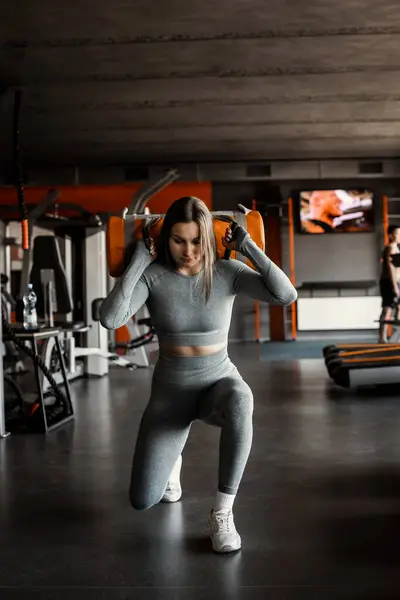Sporty young woman in grey rash guard working out with sandbag while exercises in the gym. Attractive athletic female doing hard workout with weight training with copy space for your text message.
