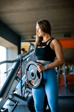Spor salonundaki formalı kız spor salonunda Demir Disk Ağırlık Levhası ile ayakta duruyor.