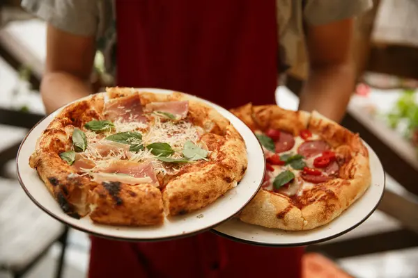 Garson elinde taze fırınlanmış baharatlı sosisli pizza tabakları tutuyor. Restoran servisi. İtalyan pizzacısı.