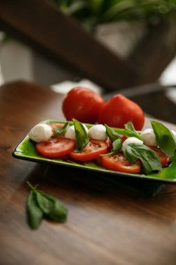 Taze mozzarella, domates ve fesleğen içeren Caprese salatası tabakta sanatsal olarak düzenlenmiş, canlı bir renk paleti ve çekici bir sunumla profesyonel yemek fotoğrafı..
