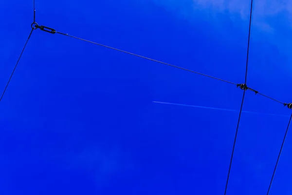 在深蓝色天空中的有轨电车线路后面 可以看到喷气式飞机的直接轨迹 电线运输线 背景图片 — 图库照片