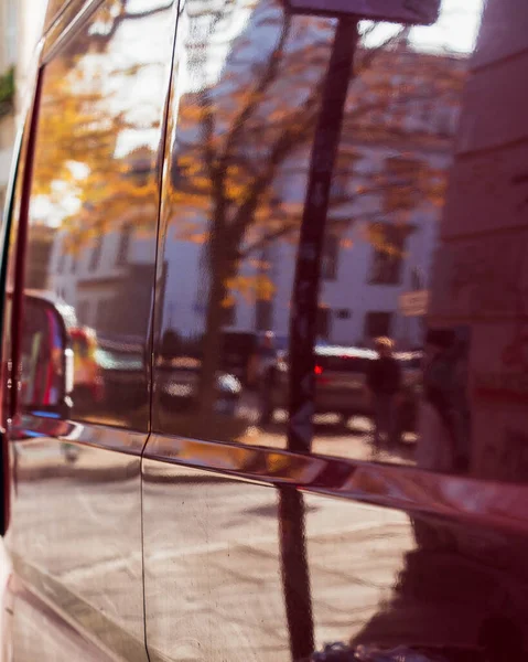 Blurred abstract autumn background of the city street is reflected on the side surface of the car. Sunny autumn background, abstract background image of a city street in bokeh, vertical orientation