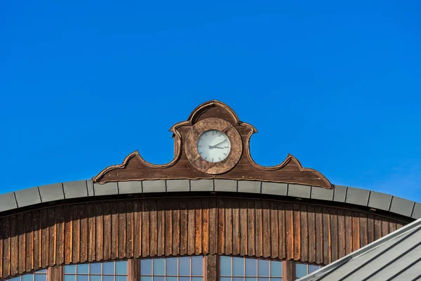 An old vintage clock on the roof of a building against a blue sky on a clear sunny day, the passage of time, the hour and minute hands show the time on a round white dial of a street clock