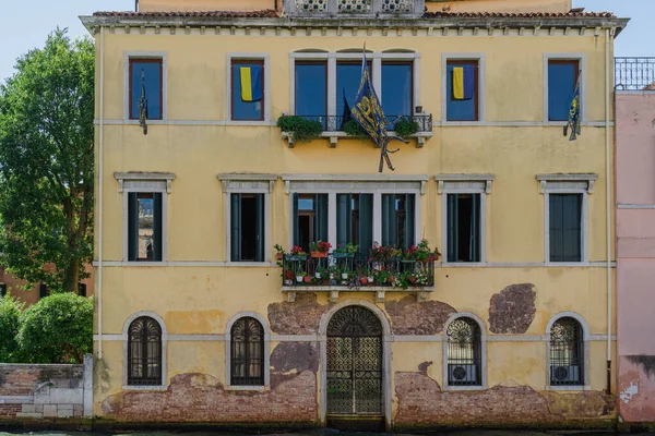 Ukrainian flags on the facade of a building in Venice, European solidarity with Ukraine. Shutters on the windows, flowers on the balconies of an old house on a Venice street canal in Italy