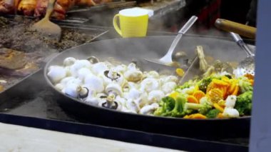 Polonya 'nın Krakow kentindeki Noel pazarındaki bir sokak kafesinde büyük bir kızartma tavasında mantar ve sebzelerin yakın çekimi. Noel ve Yeni Yıl arifesinde otantik vegan yemekleri pişirme sahnesi
