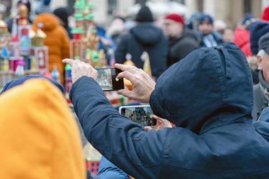 Turistler akıllı telefonlarını bir şehir caddesinde çok sayıda insan arasında halka açık bir etkinliği çekmek için kullanıyorlar. Shopka yarışması - Krakow 'un merkezinde geleneksel bir el yapımı maketler sergisi