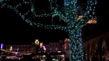 Krakow sokaklarında gece gökyüzünün arka planında parlak çelenklerle süslenmiş bir ağaç ve diğer yerler şenlikli bir Noel havası yaratıyor. Otantik Polonya Noel süslemeleri