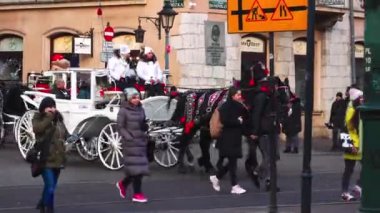 KRAKOW, POLAND - 05.12.2022: Bir kış günü, Noel simgeleriyle süslenmiş at arabaları turistleri şehir caddesinin kavşağında arabaların ve yayaların arasına taşıyor.