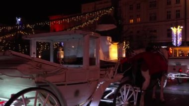 Geceleri, Krakow 'da Noel ve yılbaşından önceki gece oyuncaklarla süslenmiş ve çelenklerle süslenmiş bir şehir ağacına karşı dans eden bir çiftin silueti. Kasaba halkının siluetleri şenlikli bir sokakta
