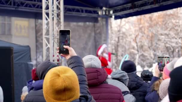 在克拉科夫 一群人欣赏一位独唱歌手在冬季平安夜装扮成雪少女的街头音乐会 在寒冷的日子里 歌迷们在街上用智能手机记录这位歌手的表演 — 图库视频影像